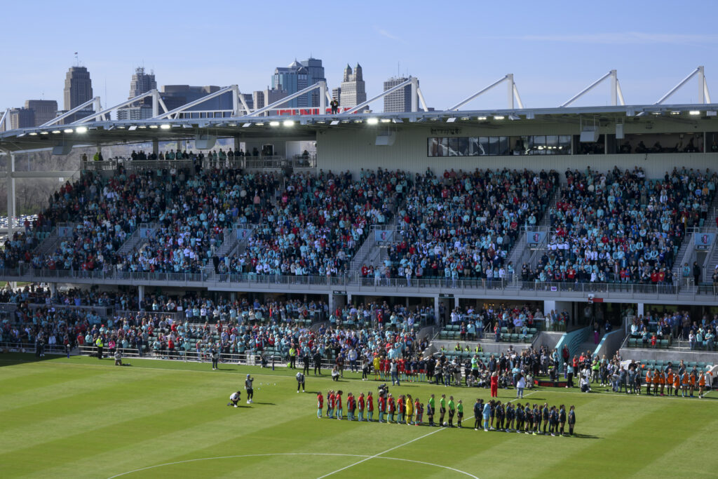 With the skyline of Kansas City behind them, both teams line up before the start of an NWSL match between the Kansas City Current and the Portland Thorns FC at the new CPKC Stadium March 16, 2024, in Kansas City, Mo. (AP Photo/Reed Hoffmann)